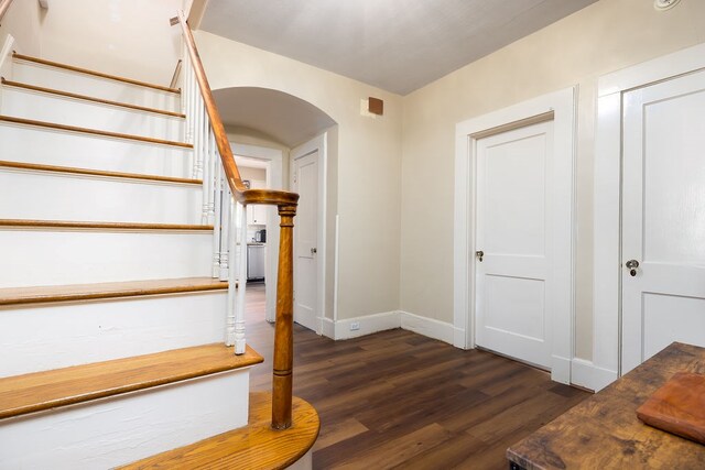 stairway featuring arched walkways, wood finished floors, and baseboards