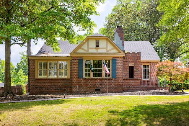exterior space with a chimney, a shingled roof, fence, a front yard, and brick siding
