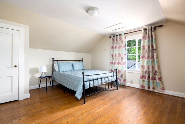 bedroom with attic access, vaulted ceiling, hardwood / wood-style floors, and baseboards