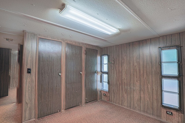 carpeted spare room featuring a textured ceiling and wood walls