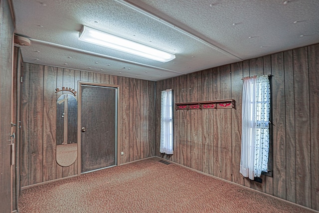 carpeted spare room with wooden walls and a textured ceiling