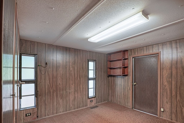 unfurnished room featuring carpet floors, a textured ceiling, and wood walls