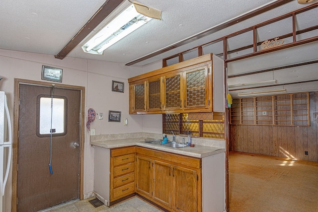 kitchen featuring wood walls, beamed ceiling, sink, white fridge, and a textured ceiling