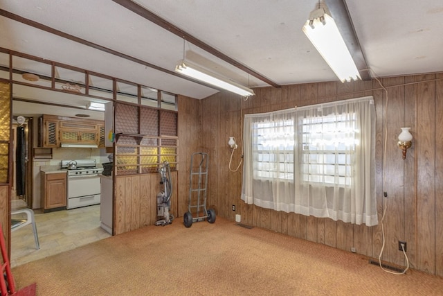 empty room featuring wooden walls, light colored carpet, and beamed ceiling