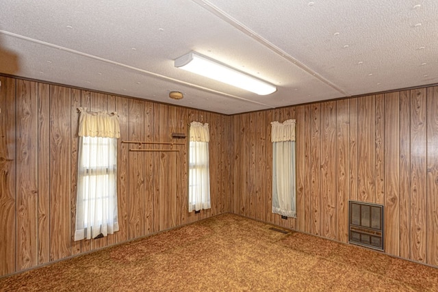 carpeted empty room featuring a textured ceiling and wood walls