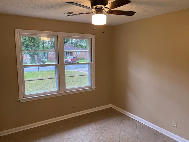 spare room featuring ceiling fan, light tile patterned floors, and a textured ceiling