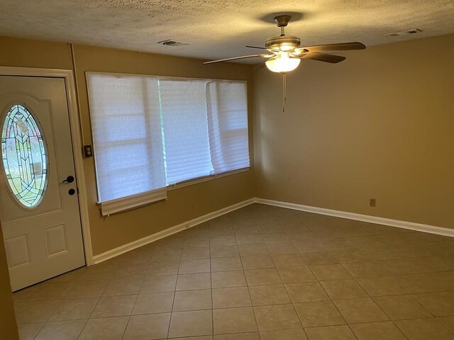 foyer entrance with ceiling fan, light tile patterned floors, and a textured ceiling