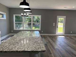 kitchen featuring light stone countertops, dark wood-type flooring, an inviting chandelier, pendant lighting, and a kitchen island