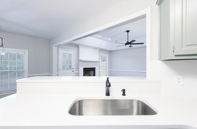 kitchen featuring ceiling fan, light countertops, a large fireplace, a sink, and a wealth of natural light