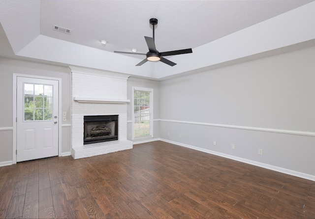 unfurnished living room with visible vents, a brick fireplace, wood finished floors, baseboards, and ceiling fan