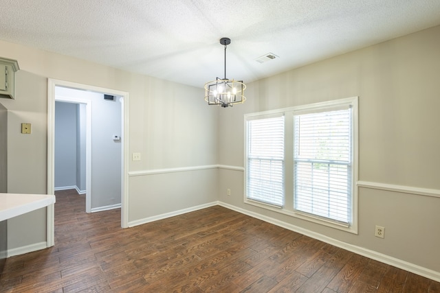 empty room with an inviting chandelier, a textured ceiling, dark wood finished floors, and baseboards