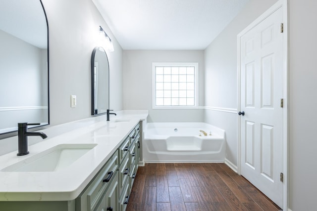 bathroom with double vanity, a sink, a garden tub, and hardwood / wood-style floors