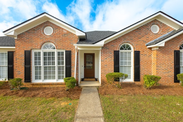 ranch-style home with brick siding, a shingled roof, and a front lawn