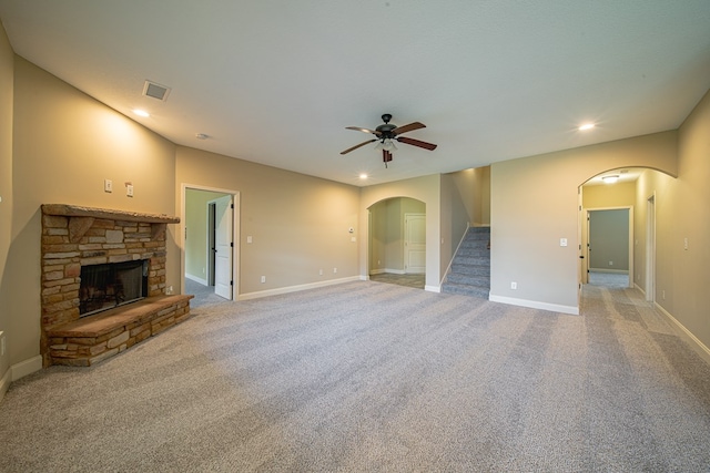 unfurnished living room with visible vents, arched walkways, light colored carpet, and a stone fireplace