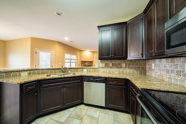 kitchen featuring dark brown cabinets, light stone countertops, decorative backsplash, appliances with stainless steel finishes, and a sink