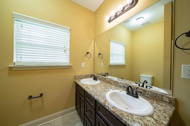 bathroom featuring visible vents, toilet, a sink, double vanity, and baseboards