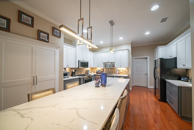 kitchen featuring stainless steel appliances, white cabinets, light stone counters, and decorative light fixtures