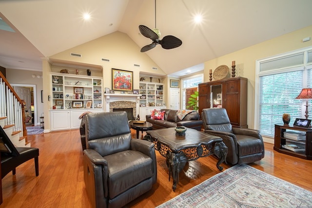 living room featuring ceiling fan, hardwood / wood-style floors, high vaulted ceiling, a fireplace, and built in shelves