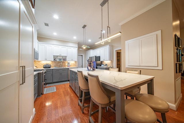 kitchen featuring stainless steel appliances, hanging light fixtures, white cabinets, and backsplash