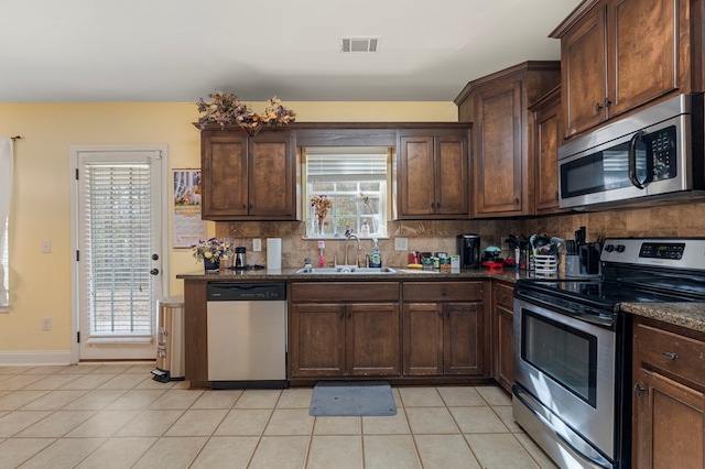 kitchen featuring tasteful backsplash, sink, light tile patterned floors, dark brown cabinetry, and stainless steel appliances