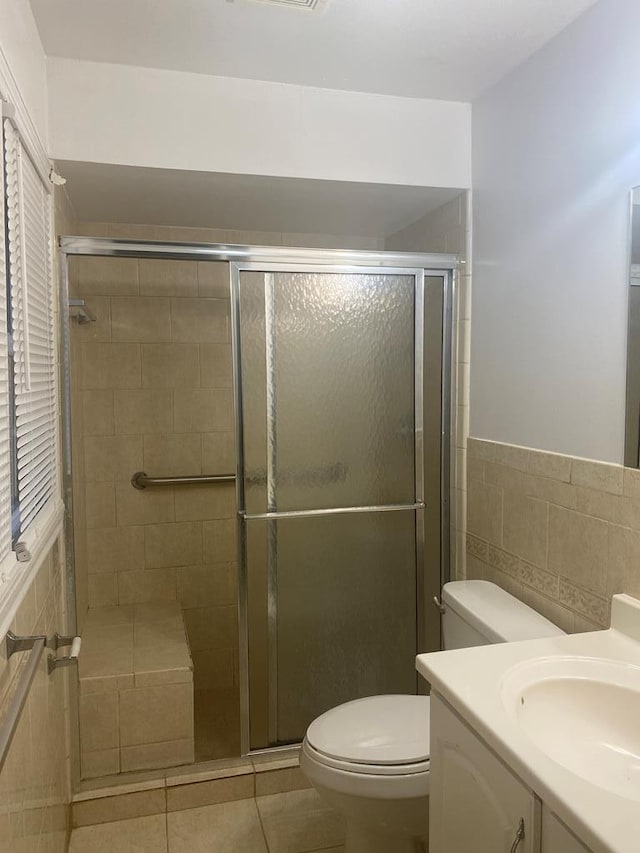 full bathroom with toilet, vanity, tile walls, a shower stall, and tile patterned floors