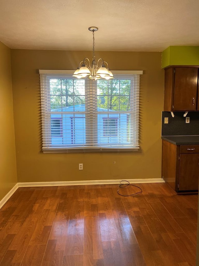 unfurnished dining area with an inviting chandelier, baseboards, and dark wood-style flooring