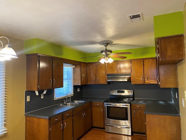 kitchen with visible vents, dark countertops, stainless steel range with electric cooktop, under cabinet range hood, and a sink