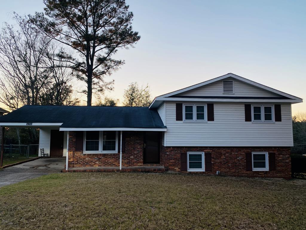 split level home featuring aphalt driveway, a front lawn, an attached carport, and brick siding