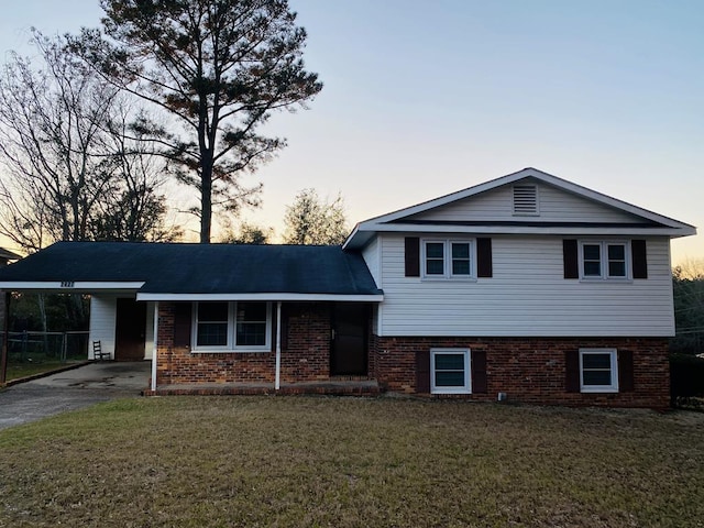 split level home featuring aphalt driveway, a front lawn, an attached carport, and brick siding