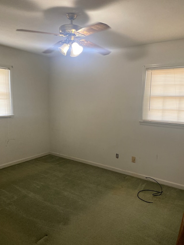 empty room with dark colored carpet, a ceiling fan, and baseboards