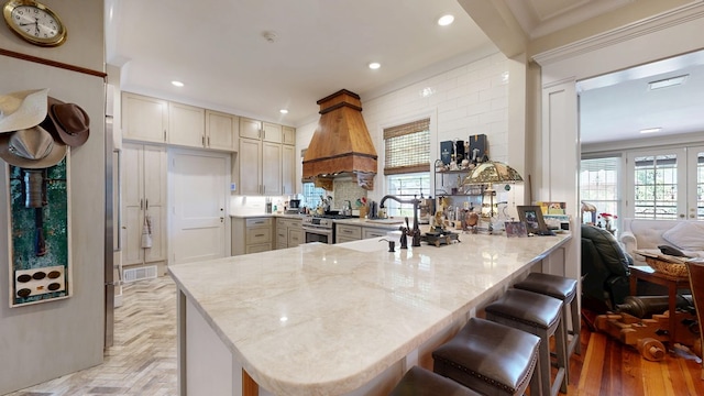 kitchen with plenty of natural light, visible vents, light stone countertops, custom exhaust hood, and a peninsula