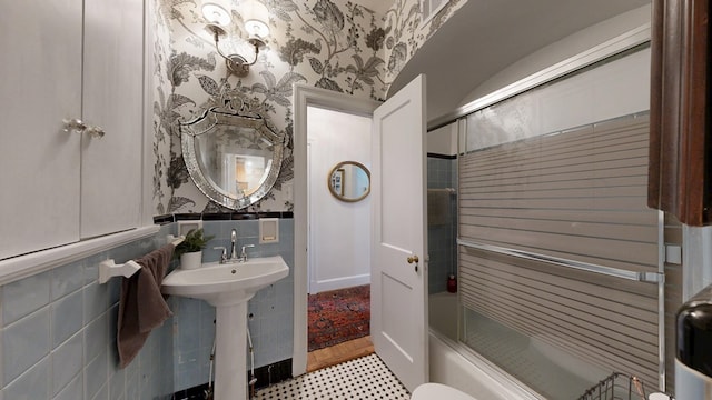 bathroom with wallpapered walls, combined bath / shower with glass door, and tile walls