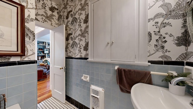 bathroom with a sink, a wainscoted wall, tile walls, and wallpapered walls