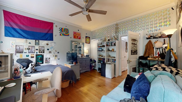 bedroom featuring light wood-type flooring, ornamental molding, a ceiling fan, and wallpapered walls