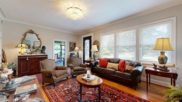 living area with baseboards, ornamental molding, wood finished floors, and a chandelier