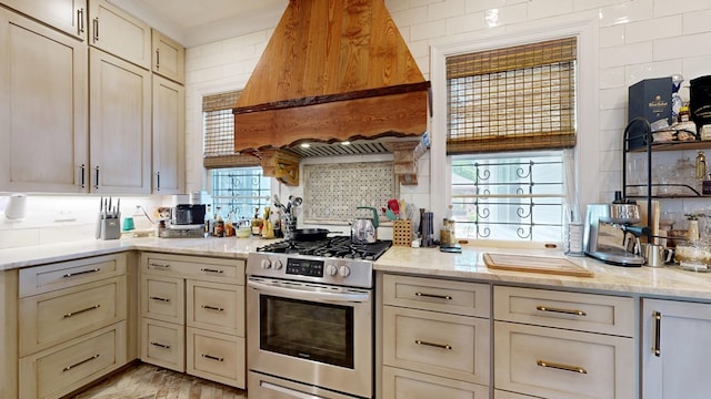 kitchen featuring stainless steel range with gas stovetop, light stone counters, cream cabinets, and premium range hood