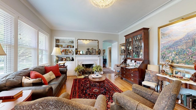 living area featuring ornamental molding, built in features, wood finished floors, a fireplace, and arched walkways