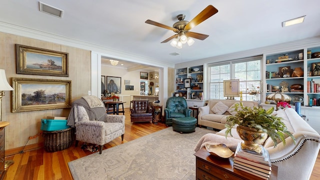 sitting room with a ceiling fan, visible vents, ornamental molding, and wood finished floors