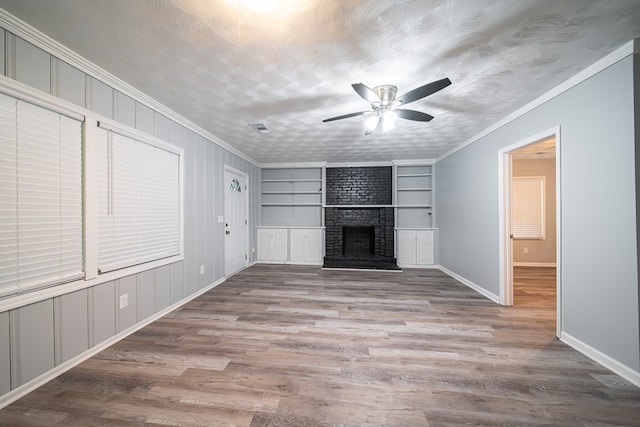 unfurnished living room with ceiling fan, built in features, crown molding, a fireplace, and light wood-type flooring