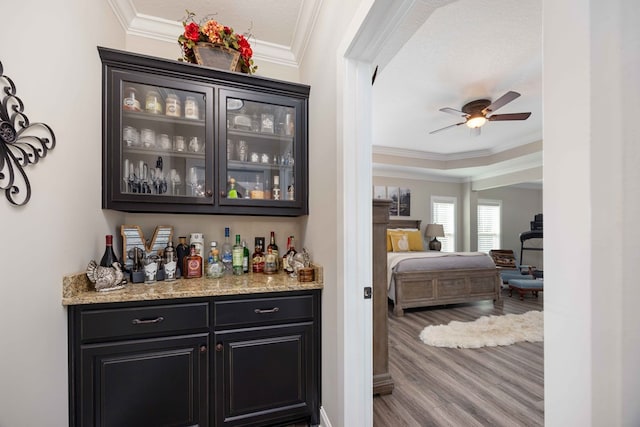 bar featuring ceiling fan, light stone countertops, ornamental molding, and light hardwood / wood-style flooring