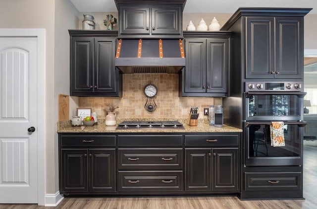 bar with light wood-type flooring, stainless steel gas cooktop, double oven, and wall chimney exhaust hood