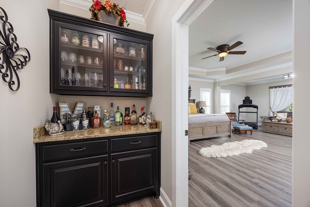 bar featuring light stone countertops, hardwood / wood-style floors, ceiling fan, and ornamental molding