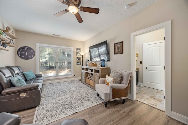 living room featuring ceiling fan, a textured ceiling, and light hardwood / wood-style flooring