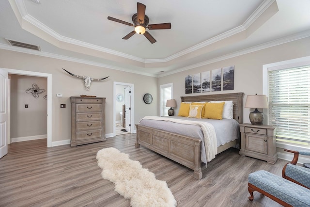 bedroom featuring ceiling fan, crown molding, a tray ceiling, and multiple windows