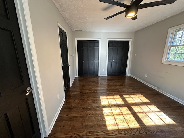 unfurnished bedroom with ceiling fan, two closets, a textured ceiling, and dark hardwood / wood-style flooring