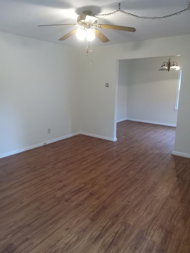 empty room with ceiling fan with notable chandelier and dark wood-type flooring