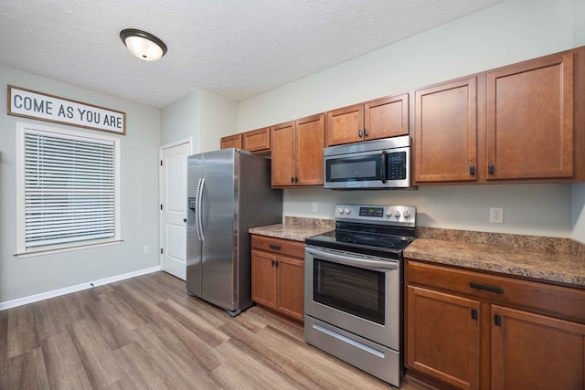 kitchen with a textured ceiling, stainless steel appliances, baseboards, light wood-style floors, and brown cabinetry