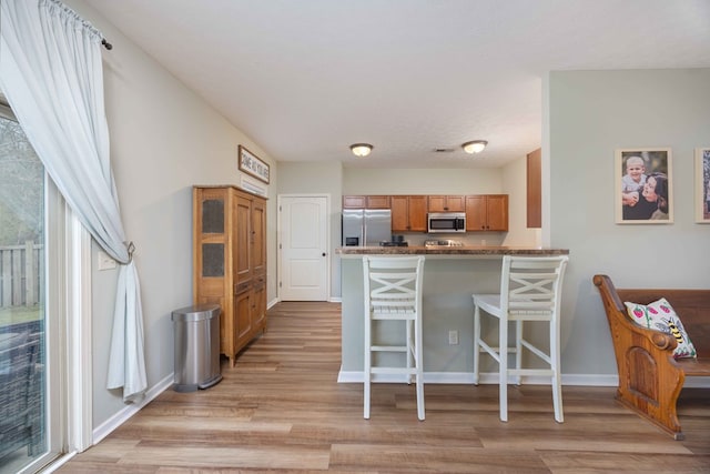 kitchen featuring a breakfast bar area, stainless steel appliances, a peninsula, brown cabinets, and dark countertops