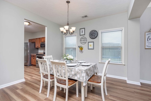 dining room with a textured ceiling, light wood-style flooring, visible vents, and baseboards