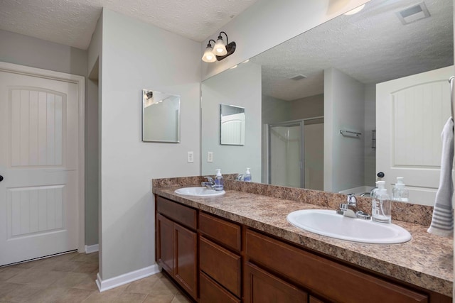 full bath with a sink, a shower stall, a textured ceiling, and double vanity